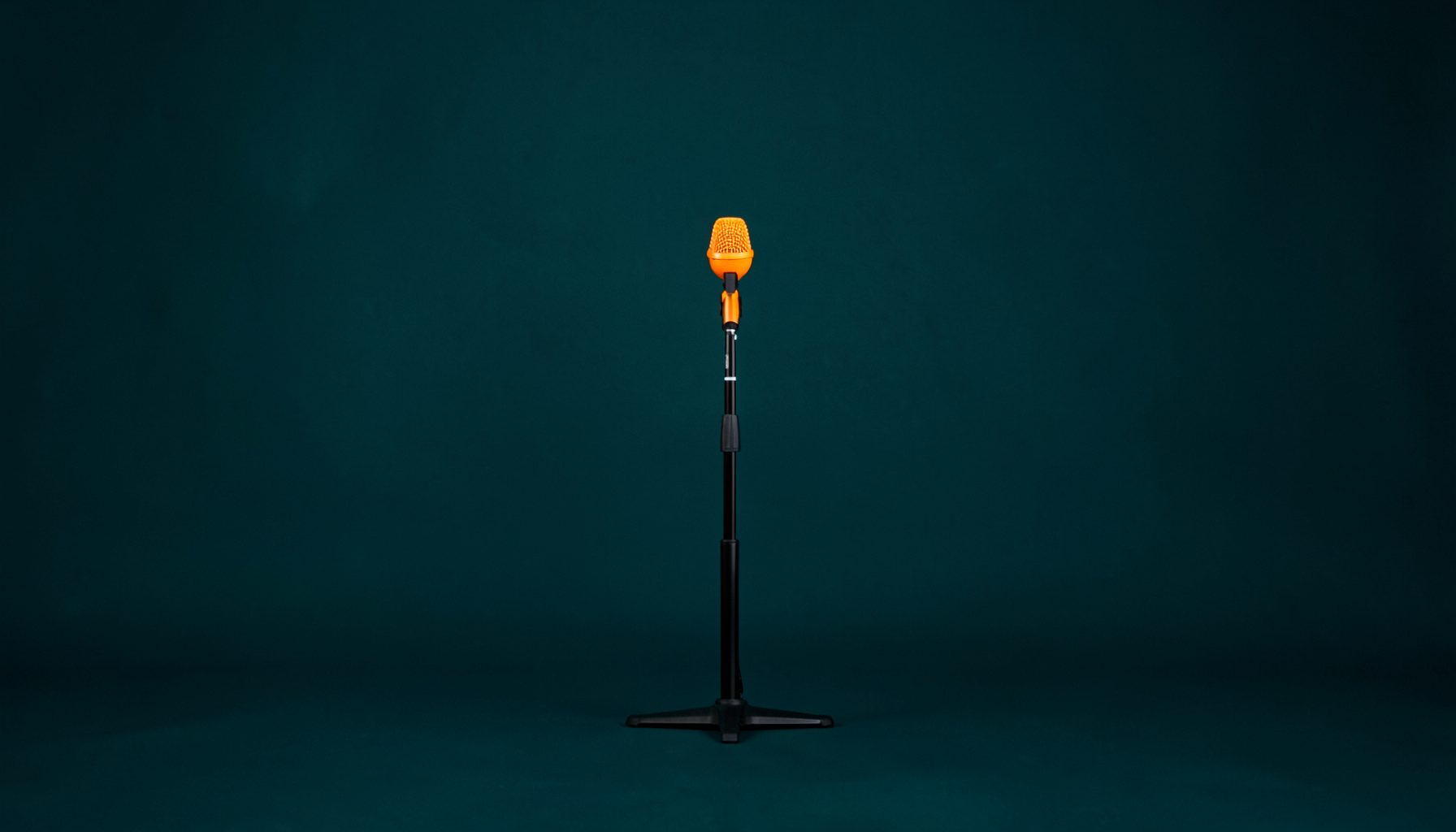 Small square photograph of a microphone stand centered symmetrically against a dark teal backdrop, quiet mood