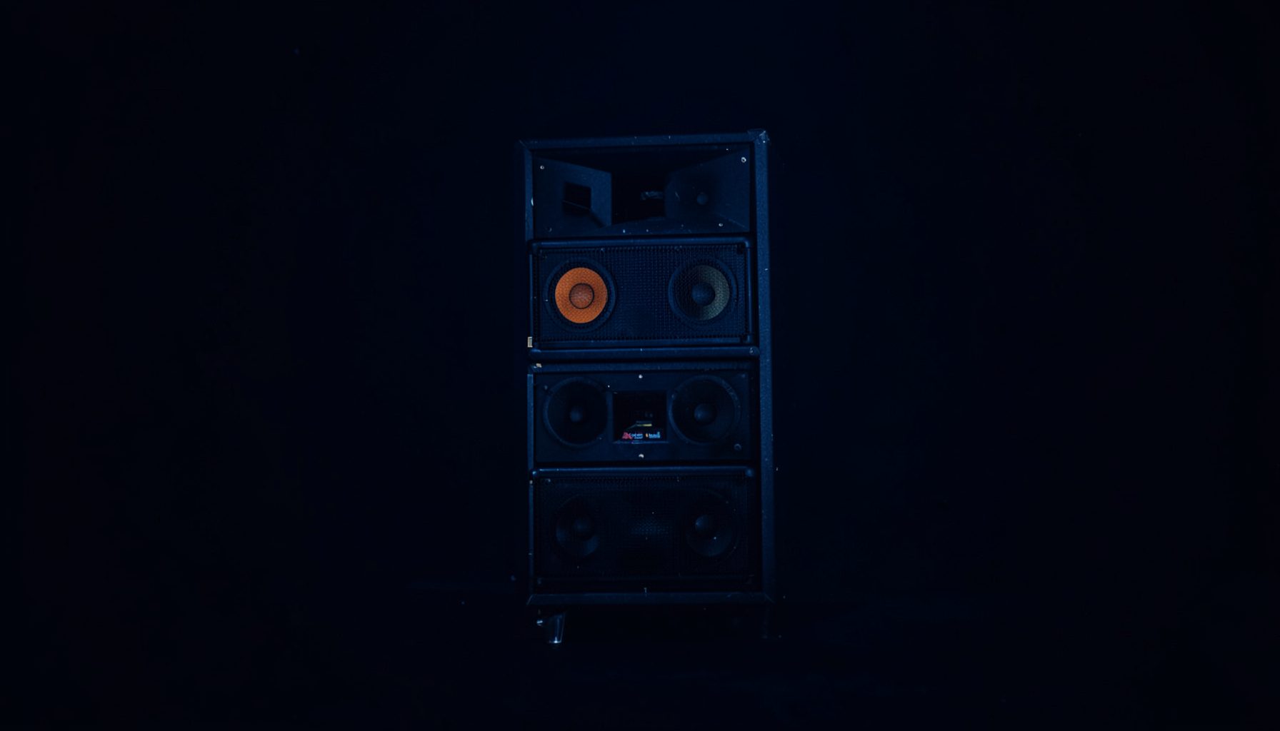 Small square photograph of stacked concert speakers in deep navy shadow with a moody atmosphere